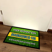 Fußmatte Rasenoptik für Fußball Fans | Hier wohnt ein Braunschweig Fan - Betreten an Spieltagen auf eigene Gefahr! | Türmatte mit Spruch | 60x40cm | für innen und außen | Vorleger für Haustür / Flur